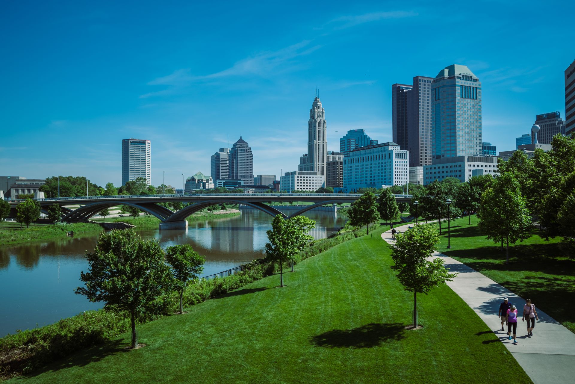Ohio riverfront park on a clear summer day, downtown towers beyond the bridge